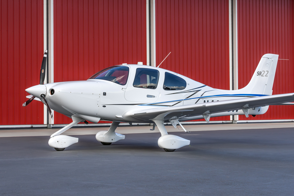 The Cirrus SR22T is a high-performance, single-engine, four-seat propeller airplane produced by Cirrus Aircraft.  The company headquarters is located in Duluth, Minnesota.   The left front quarter view of the airplane showcases its modern design with its sleek aerodynamics .   The airplane's pearl white paint contrasts nicely against  the darker, barn red painted hangar in the background.  This photo was taken in June 2024 at the Renton Municipal Airport, Washington.